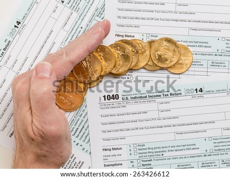 Caucasian hand protecting wealth in solid gold eagle coins on USA tax form 1040 for year 2014 illustrating keeping assets away from the IRS