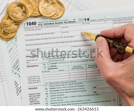 Caucasian hand with pen and solid gold eagle coins on USA tax form 1040 for year 2014 illustrating payment of taxes on forms for the IRS