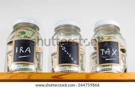 Three glass jars with chalk labels used for saving US dollar bills and notes for IRA, tax and college funds