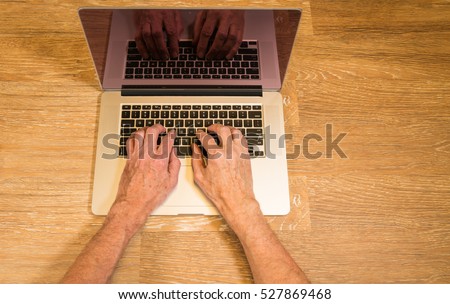 Senior caucasian adult man types on modern keyboard of laptop or ultrabook on wooden desk with copy space