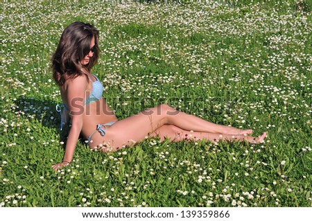 Young girl in bikini sitting on the lawn with wildflowers
