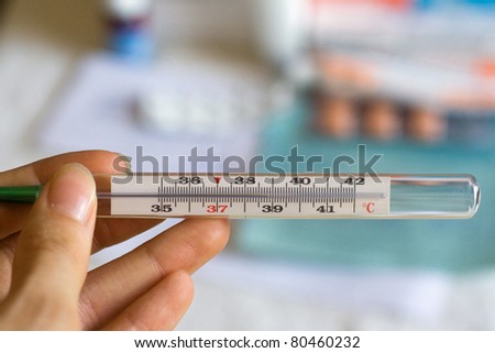 Woman's hand holding clinical thermometer indicating a high temperature