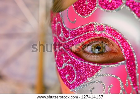 Close-up photo from a beautiful female eye with a venetian mask, with a venetian umbrella in the background/woman in mask