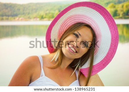 Beauty and the hat / Beautiful young woman standing before a lake in a colorful big hat