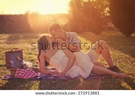 Attractive Couple Enjoying Romantic Sunset Picnic in the Countryside / Vintage style photo with custom white balance, color filters, strong but beautiful lens flare, and some fine film grain added