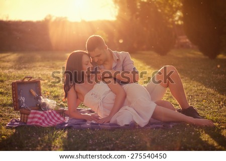 Attractive Couple Enjoying Romantic Sunset Picnic in the Countryside / Vintage style photo with custom white balance, color filters, strong but beautiful lens flare, and some fine film grain added