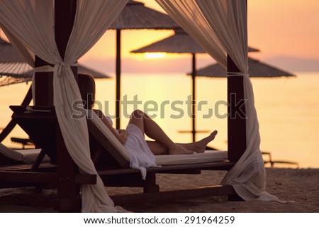 Resting in the beach / Beautiful young women resting in a beach, sunrise over the sea in the background, with custom white balance, soft focus effect, and some fine film grain added