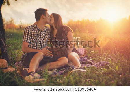 Attractive Couple Enjoying Romantic Sunset Picnic in the Countryside / Vintage style photo with custom white balance, color filters, and some fine film grain added