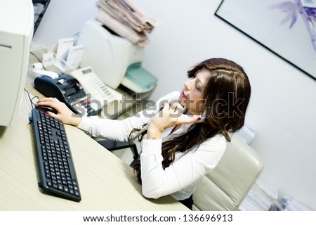 young business woman talking at the phone sitting at the desk on office background