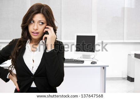 Young surprised business woman talking ah the phone on office background