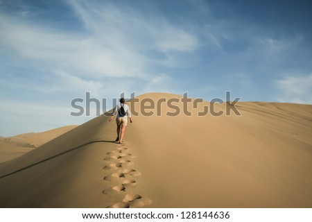 A woman walks alone through desert sand dunes in the Taklamakan desert near Dunhuang, China