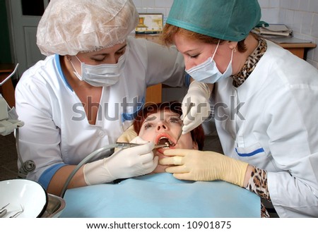 Woman with open mouth look at doctor. Doctor to drill a tooth. Nurse to help a doctor.
