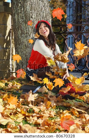 young woman with notebook sits under tree, on fall leafs background