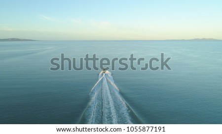 AERIAL: Fishing boat leaves a trail in the calm ocean water as it speeds towards endless horizon on a picturesque summer day. Flying behind fisherman speeding in small boat into the vast open ocean.