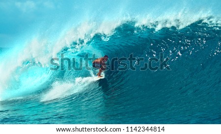 CLOSE UP: Young pro surfer surfs a big barrel wave in popular surf spot in breathtaking Tahiti. Awesome view of a extreme surfboarder riding epic blue waves in the hot summer sun of French Polynesia.