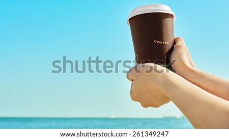 Woman hands handling paper coffee cup near the blue sea
