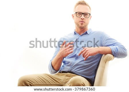 Talking young man. Portrait of handsome young man in casual blue shirt and dioptrical glasses sitting in comfortable pose isolated on white background