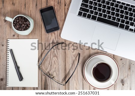 office working desk top view with laptop, notepad, glasses, smartphone and coffee cup