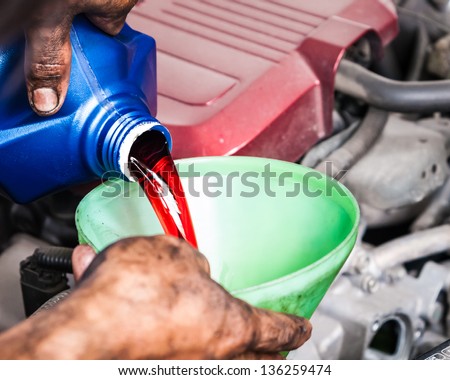 Hand pouring transmission fluid through funnel as for the good car maintenance