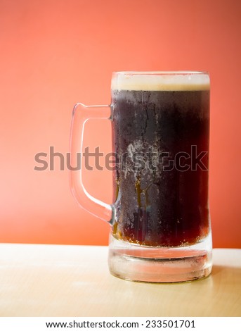Cold root beer on top of wooden table in front of orange background