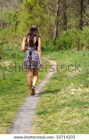 Back view of a teenage girl walking along a gravel path in the woods.