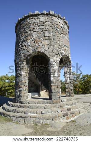 round observation tower at Mount Battie in Camden, Maine.  The structure is round and made of stones with an inside spiral staircase. There is a beautiful blue sky above the tower.