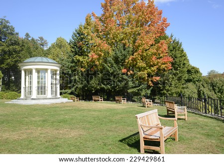 round gazebo and wood park benches by a black iron fence.  There is a grass area and trees, with leaves starting to change colors