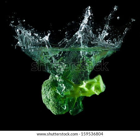 Green broccoli falling in water on white with air bubbles
