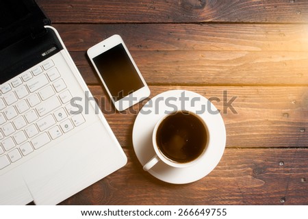 Office desk with laptop computer, notebook, mobile smartphone and coffee cup on wood,morning light