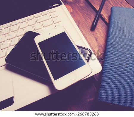 Office desk with laptop computer, notebook, mobile smartphone and pen on wood,vintage color toned image