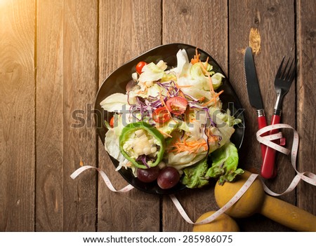 Dumbells, tape measure and healthy food salad on wooden background,View from above