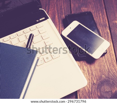 Office desk with laptop computer, notebook, mobile smartphone and pen on wood,vintage color toned image