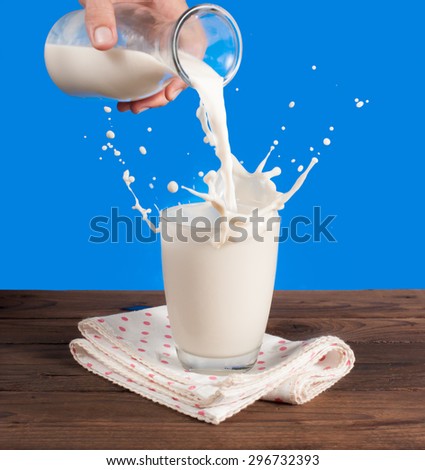 Milk from a jug pouring into glass on a blue background