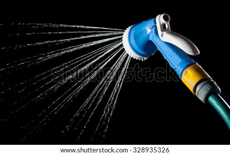 Hose nozzle spraying water on dark background