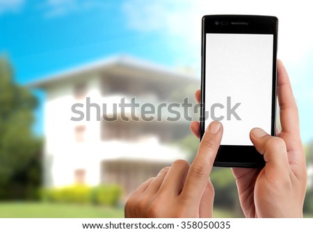 Hand holding smart phone on blured white house background.
