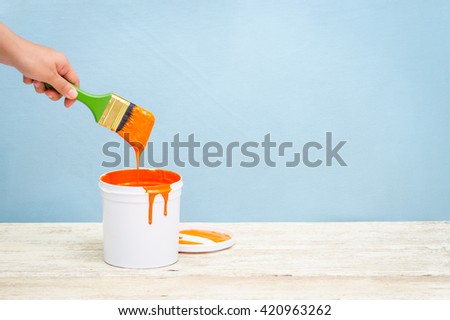 Hand holding the paint brush and White plastic bucket with orange color on wood,vintage background