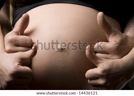 Close-up of a belly with the hands of the happy future parents with thumbs up