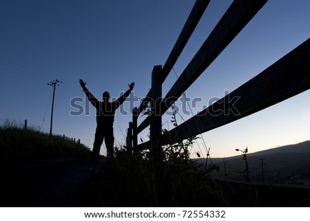 Silhouette of a young Man with his Hands up and perspective view of a Fence