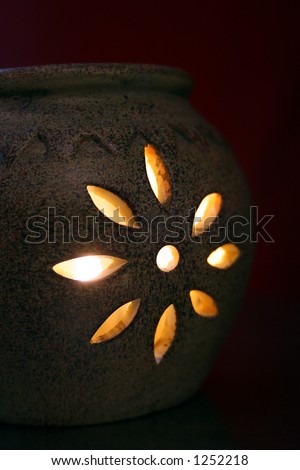 Ceramic candle holder with flower cut out and lit votive against dark red wall.