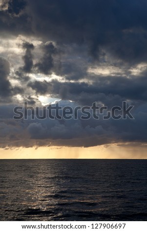 A dramatic set of clouds drifting over the tropical waters of the Caribbean Sea are lit by the last moments of daylight.