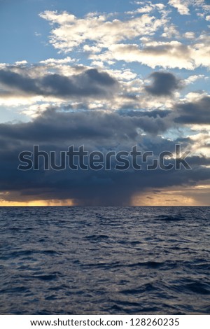 A large cloud dumps rain onto the warm waters of the Caribbean Sea at sunrise.