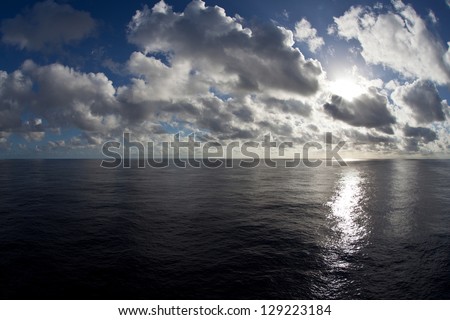 Drifting cumulus clouds are lit by the rising sun as they pass over the calm waters of the tropical South Pacific Ocean.