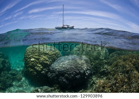 A small yacht cruises close to a shallow coral reef near New Caledonia in the South Pacific Ocean.
