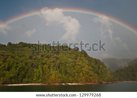 A full rainbow arches over a jungle-covered island in the Mergui Archipelago, Myanmar.  This area is known for its scuba diving.