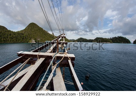 The bow of a Pinisi schooner, working as a diving liveaboard, points towards a set of idyllic limestone islands in Wayag, Raja Ampat, Indonesia. This region is known for its high marine diversity.