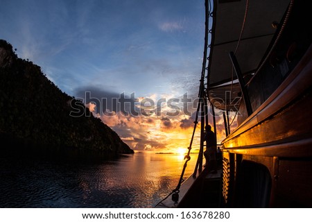 A Brilliant Sunset Lights Up The Sky, The Sea, And An Indonesian Pinisi Schooner Used As A Diving Live Aboard In Raja Ampat, Indonesia. This Region Harbors Fantastic Scuba Diving And High Diversity.