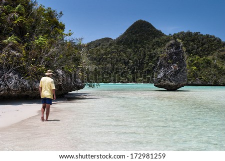 In Raja Ampat, Indonesia, a man walks along a white sand beach in Wayag, just above the equator, where limestone  islands have been eroded into the various shapes that people currently admire.