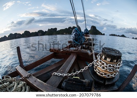 The bow sprit of an Indonesian Pinisi schooner points at a set of remote limestone islands in  Raja Ampat, Indonesia. This type of double-masted, wooden ship is often seen and used in Indonesia.
