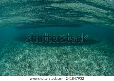 A small boat creates a dark shadow on the Caribbean seafloor as it floats in shallow water.