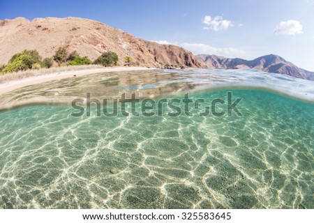 Sunlight ripples across a shallow, sandy seafloor fringing an arid island in Komodo National Park, Indonesia. This area harbors high marine biodiversity and is a popular destination for divers